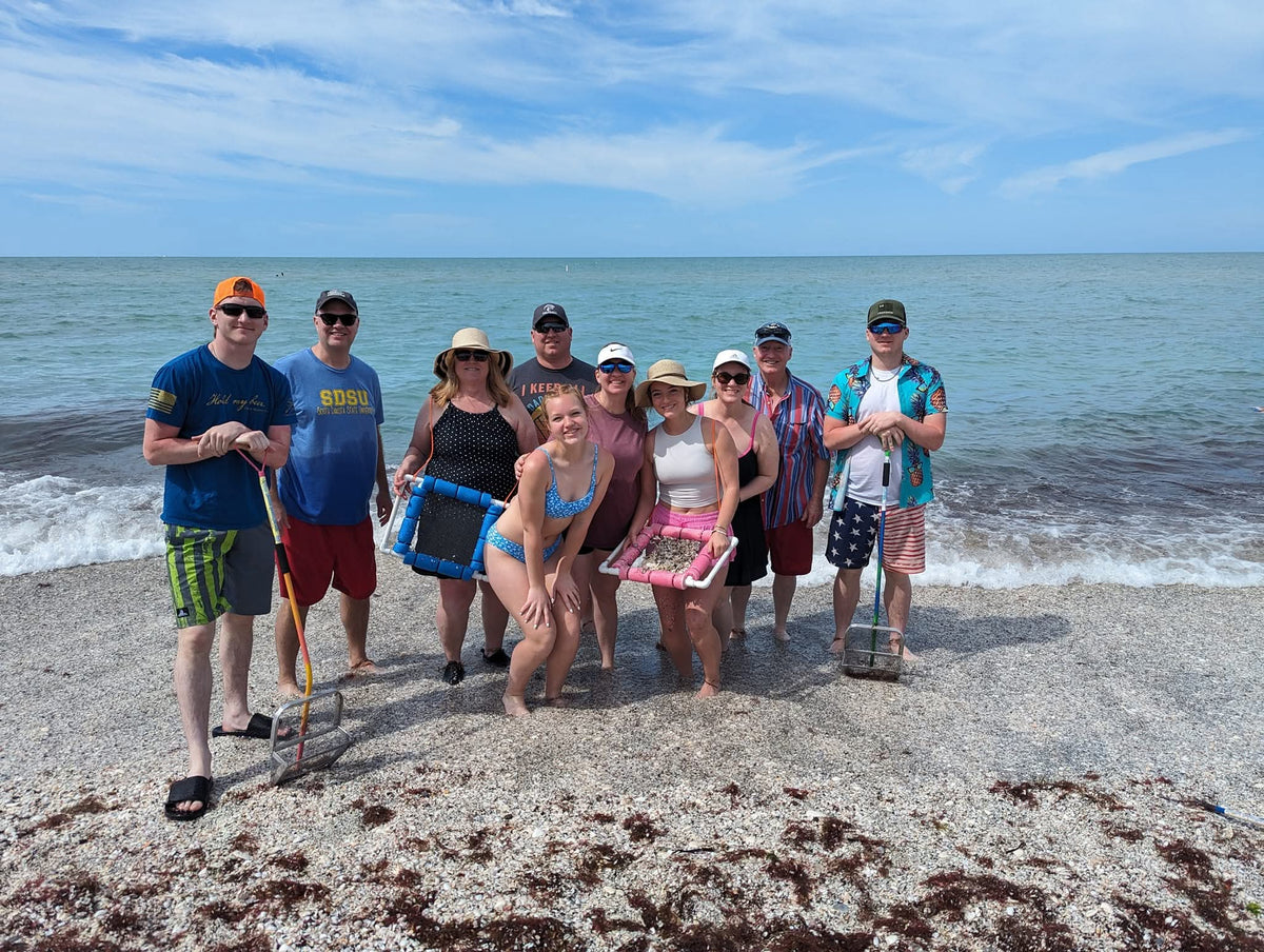 Large group of tourists. very happy by the water after shark tooth hunting, holding a floating sifter in their hand posing for a picture