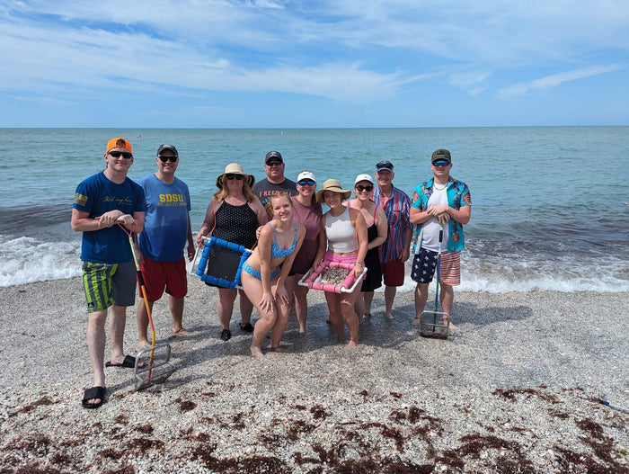 Large group of tourists. very happy by the water after shark tooth hunting, holding a floating sifter in their hand posing for a picture